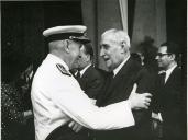 Fotografia do Presidente da República Américo Tomás, acompanhado por Gertrudes Rodrigues Tomás, abraçando Oliveira Salazar durante a partida para a visita de estado a Moçambique, na Gare Marítima de Alcântara, em Lisboa.