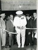 Fotografia de Américo Tomás, acompanhado por António Augusto Peixoto Correia, cortando uma fita durante uma cerimónia de inauguração, por ocasião da visita de estado efetuada a Moçambique