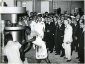 Fotografia de Américo Tomás, acompanhado por António Augusto Peixoto Correia, numa fábrica de tambores em Luanda, por ocasião de uma paragem de três dias em Angola, durante o regresso da visita de estado efetuada a Moçambique