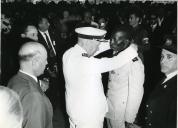 Fotografia de Américo Tomás, acompanhado por António Augusto Peixoto Correia, no distrito de Gaza, condecorando um militar, por ocasião da visita de estado efetuada a Moçambique