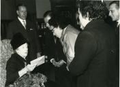 Fotografia de Gertrudes Rodrigues Tomás recebendo um ramo de flores e uma carta no interior de um edifício por um grupo de civis