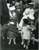 Fotografia de Américo Tomás, acompanhado por Gertrudes Rodrigues Tomás, beijando uma criança por ocasião da visita oficial efetuada ao distrito da Guarda, entre o dia 30 de maio e o dia 2 de junho de 1964