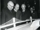 Fotografia de Américo Tomás, acompanhado por José João Gonçalves de Proença, observando uma maqueta da ponte sobre o rio Tejo, durante a inauguração de uma nova sede do Grémio das Indústrias Panificadoras em Lisboa