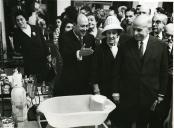 Fotografia de Américo Tomás, acompanhado por Gertrudes Rodrigues Tomás e por José João Gonçalves de Proença, no Stand C. Santos, por ocasião da inauguração de uma exposição de enfermagem