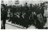 Fotografia de oficiais da Marinha portuguesa e populares à saída do Mosteiro de Santa Maria de Belém (Mosteiro dos Jerónimos), para assistir ao início da procissão realizada por ocasião da cerimónia da missa e bênção dos navios bacalhoeiros