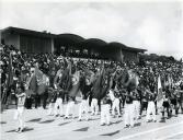 Fotografia de Américo Tomás assistindo a um desfile de atletas no estádio universitário da Faculdade de Coimbra, por ocasião das celebrações do IX Centenário da Reconquista Cristã da Cidade de Coimbra