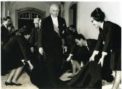 Fotografia de Américo Tomás caminhando sobre capas de trajes académicos, por ocasião da sessão solene de abertura do novo ano letivo da Universidade de Coimbra