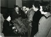 Fotografia de Gertrudes Rodrigues Tomás recebendo um ramo de flores no interior de um edifício por um grupo de civis