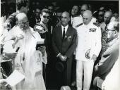 Fotografia de Américo Tomás, acompanhado por Gertrudes Rodrigues Tomás e por António Augusto Peixoto Correia, ouvindo uma figura eclesiástica discursar, por ocasião da visita de estado efetuada a Moçambique