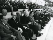 Fotografia de Américo Tomás, acompanhado por Alfredo Rodrigues dos Santos Júnior e por Inocêncio Galvão Teles, no Estádio Nacional do Jamor assistindo a um jogo de futebol entre as seleções de Portugal e Inglaterra, por ocasião da comemorações do 50.º aniversário da Federação Portuguesa de Futebol