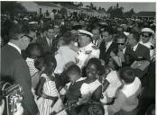 Fotografia de Américo Tomás, acompanhado por António Augusto Peixoto Correia, segurando uma criança ao colo rodeado por populares em Luanda, por ocasião de uma paragem de três dias em Angola, durante o regresso da visita de estado efetuada a Moçambique