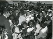 Fotografia de Américo Tomás, acompanhado por António Augusto Peixoto Correia, segurando uma criança ao colo rodeado por populares em Luanda, por ocasião de uma paragem de três dias em Angola, durante o regresso da visita de estado efetuada a Moçambique