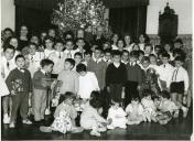 Fotografia de Américo Tomás acompanhado por Gertrudes Rodrigues Tomás no Palácio de Belém, rodeados por crianças durante as celebrações de Natal