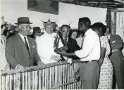 Fotografia de Américo Tomás, acompanhado por Gertrudes Rodrigues Tomás, recebendo presentes de artesãos na feira de artesanato de Paquitequete, Porto Amélia, durante a visita de estado a Moçambique