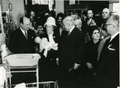 Fotografia de Américo Tomás, acompanhado por Gertrudes Rodrigues Tomás e por José João Gonçalves de Proença, no Stand C. Santos, por ocasião da inauguração de uma exposição de enfermagem